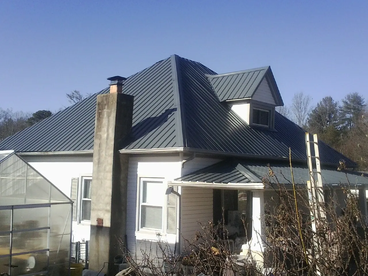 Dark blue standing seam metal roof on a white farmhouse with dormer — Slate & Tile Roof Repair by Roofing Brothers in Raleigh