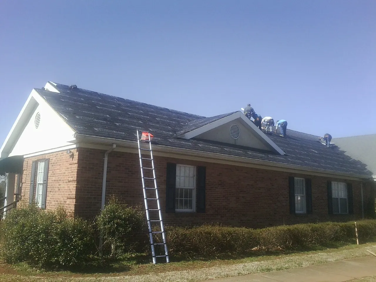 Crew tearing shingles off a brick ranch roof with a ladder set — Emergency Roof Repair work by our crew in Raleigh