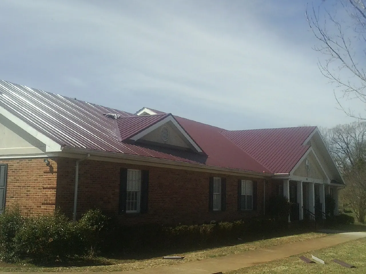 Red metal roof with gabled entries on a long brick building, from a Hail Damage Roof Repair job in Raleigh