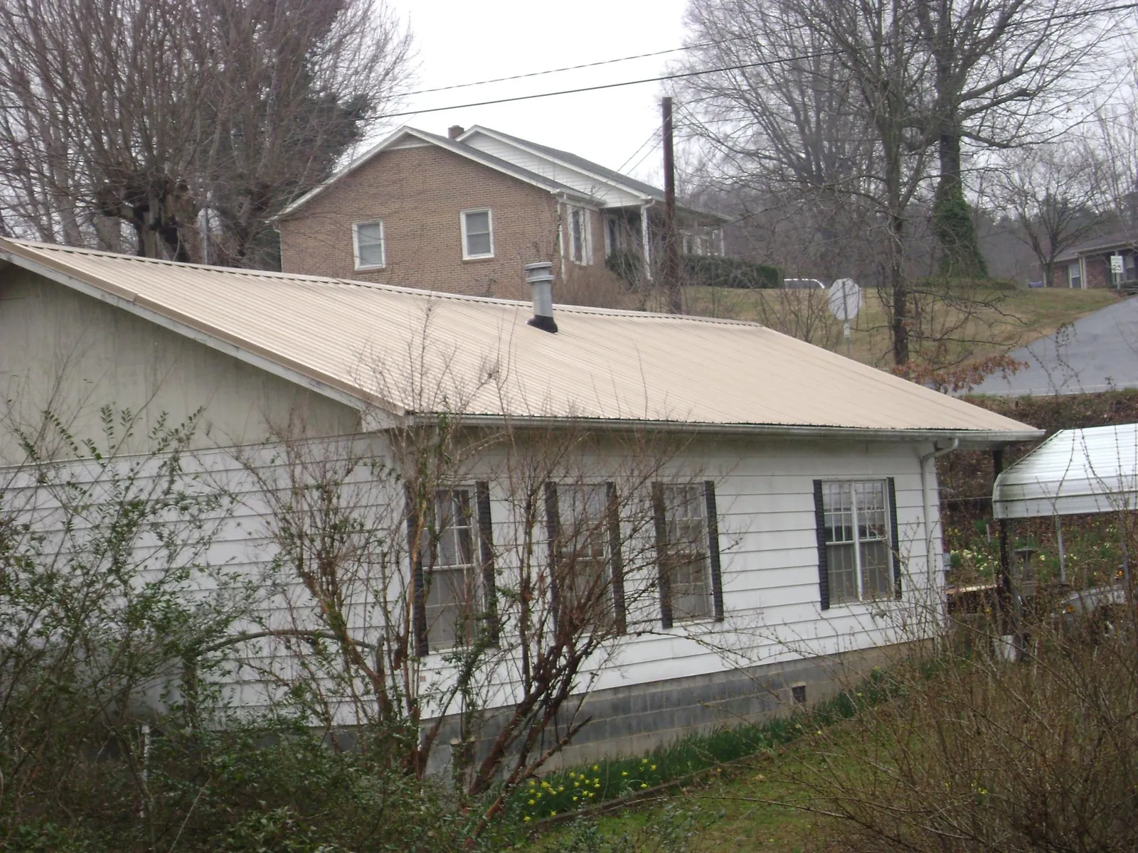 Tan metal roof on a white sided house set into a hillside — Commercial Roofing by Roofing Brothers in Raleigh