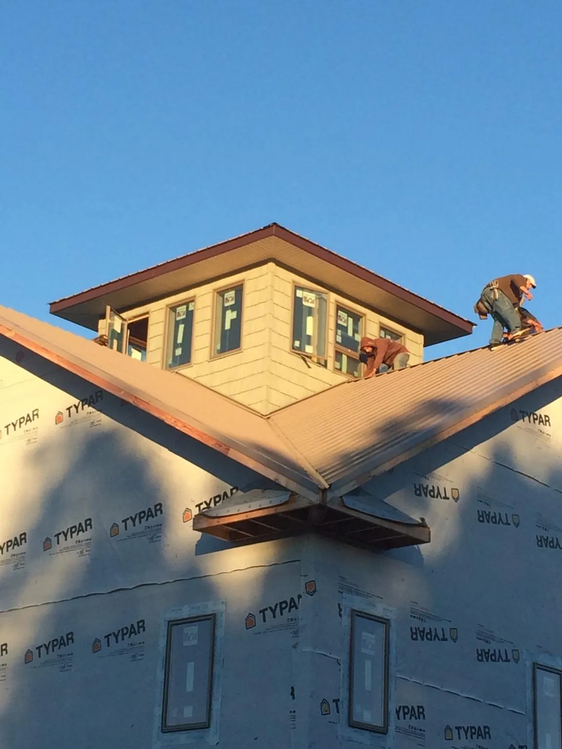 Roofers working around a rooftop cupola on a new metal roof at sunset — Roof Waterproofing in Raleigh by Roofing Brothers